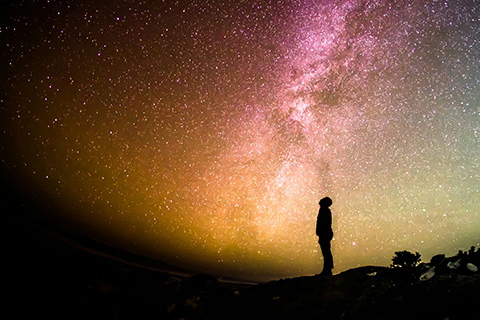 A silhouetted person stand with the cosmos above them.