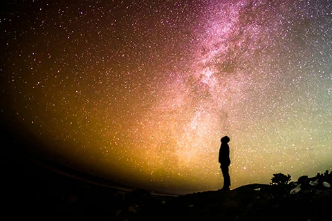 A silhouetted person stand with the cosmos above them.