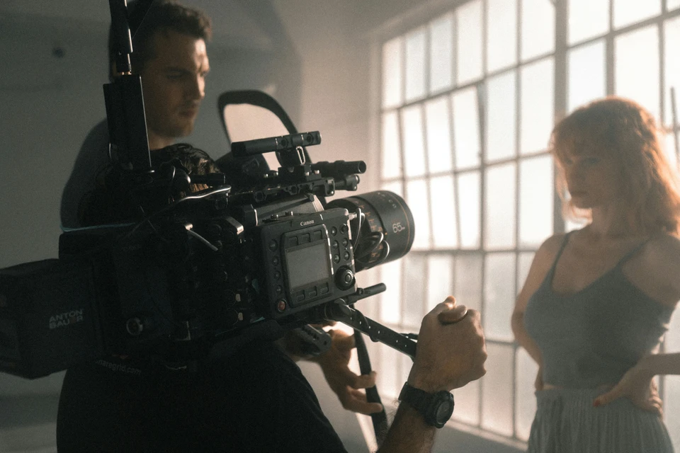 An actor is filmed in a moody room against a large bright window.