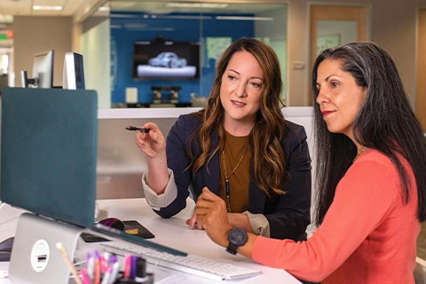 Two people at a desk discussing information displayed on a screen.