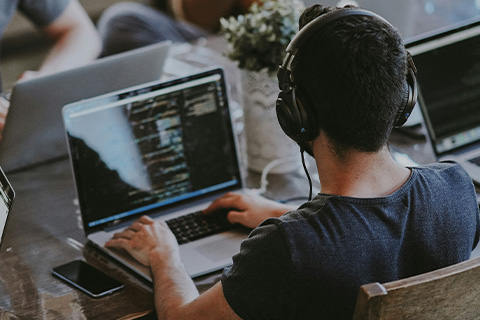 A developer sits at a table with colleagues and writes code.