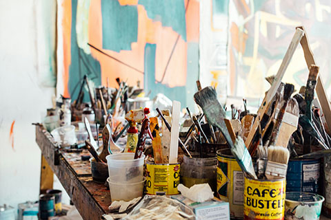 A messy art studio with pots and brushes scattered all over a table.