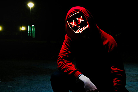A hooded figure with bright neon lights making up his eyes and mouth, lurks in the shadows.