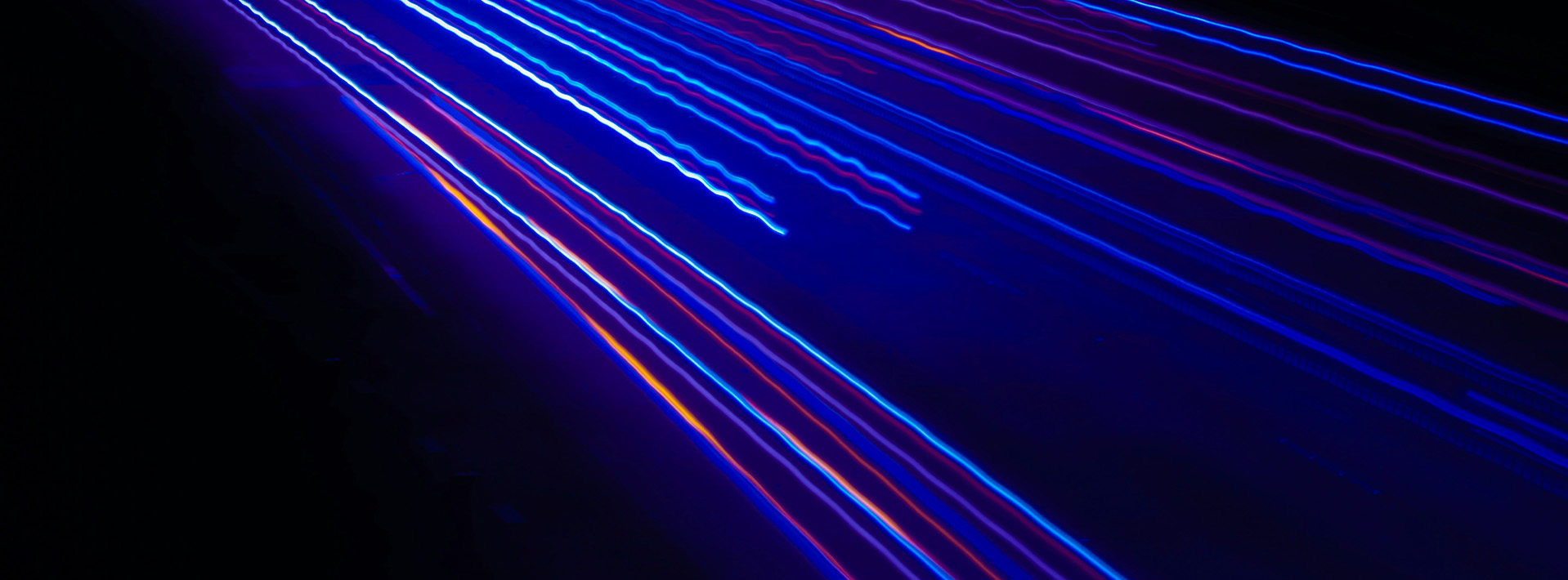 Thin traces of straight and fluctuating neon light shoot past in the dark.
