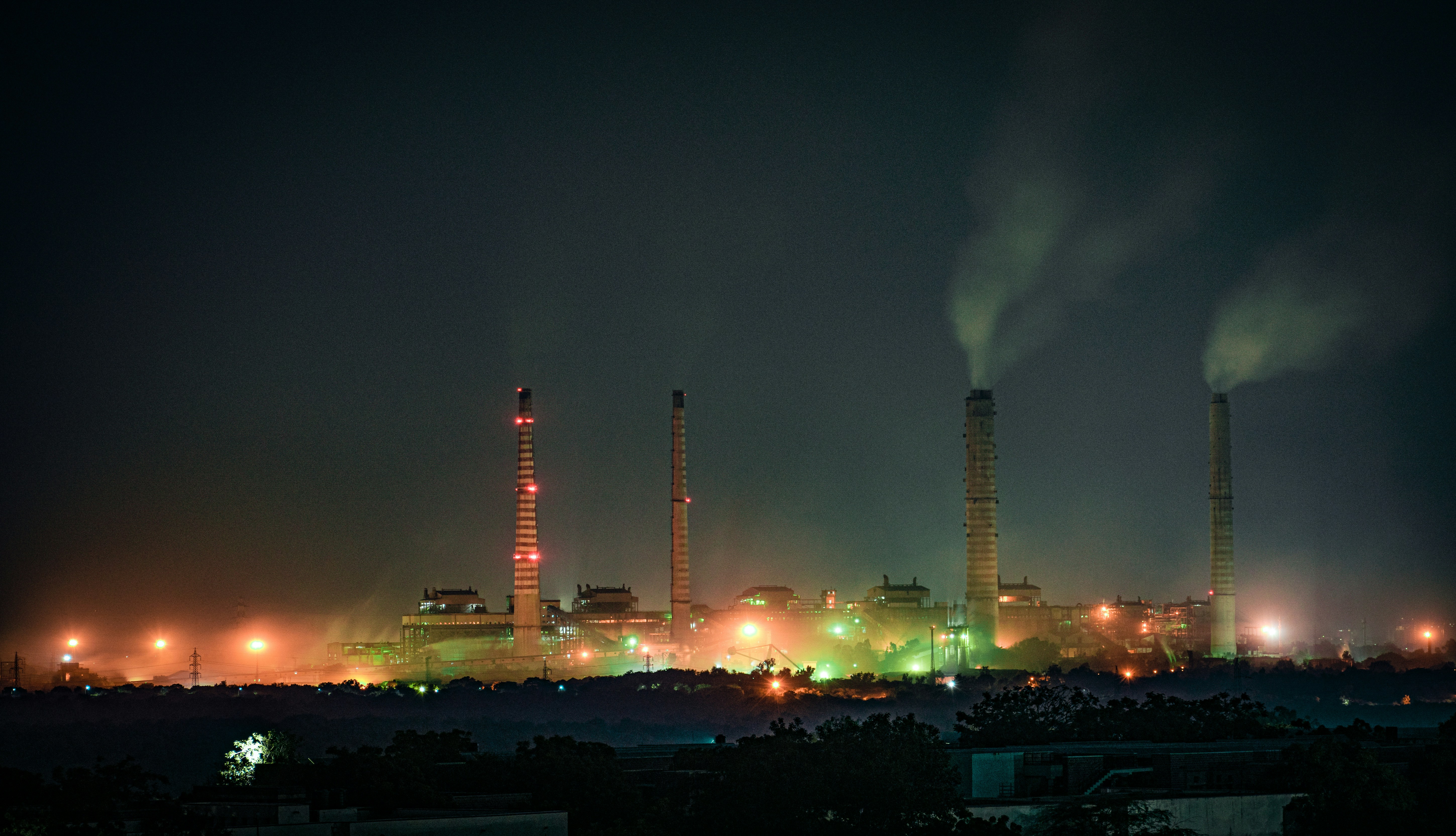 A view of an industrial plant, with smoke stacks lit up at night in glowing colours.