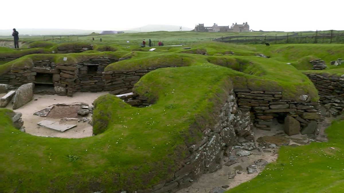 A photo of Skara Brae showing the rolling green mounds and stone structures and doorways.